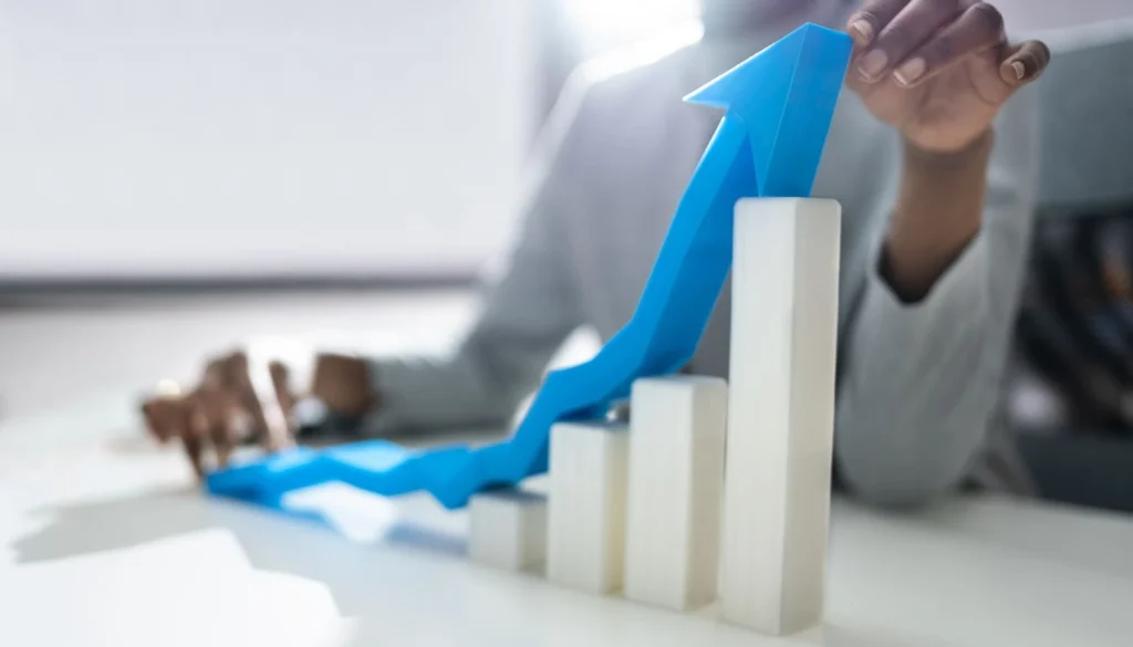 A person holding an upward-pointing blue arrow over a white bar chart on a desk, symbolizing growth in patient acquisition and the success of AI-driven marketing strategies in healthcare.